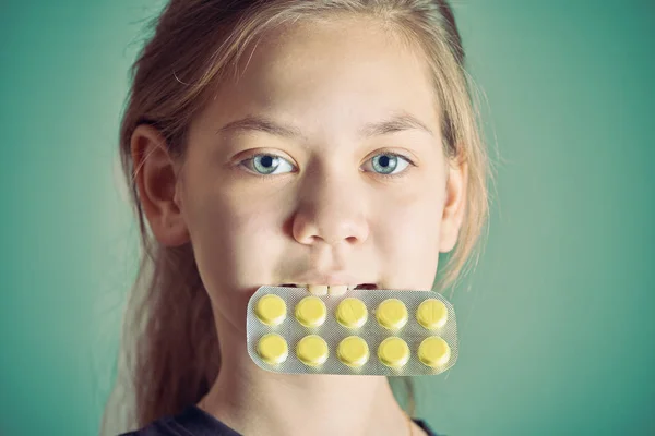 Gesundes Mädchen mit schönen Augen hält im Mund Packung mit gelben Pillen auf grünem Hintergrund. — Stockfoto