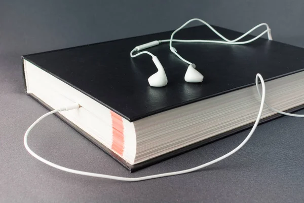 Fones de ouvido brancos jazem em um livro preto grosso — Fotografia de Stock