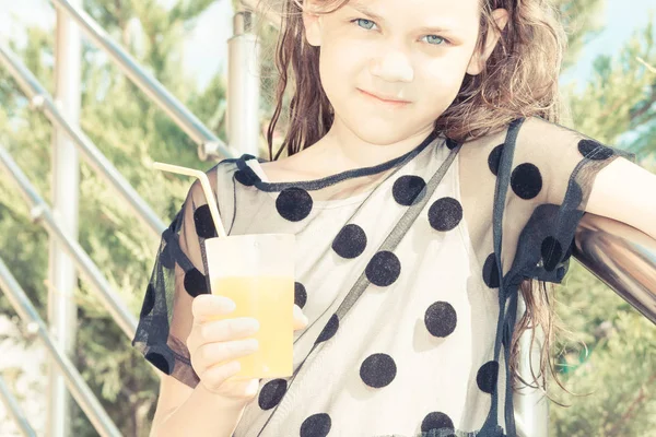 Belle fille en robe noire d'été à pois tenant le verre avec du jus et de la paille appuyé sur une rampe de fer le jour ensoleillé . — Photo