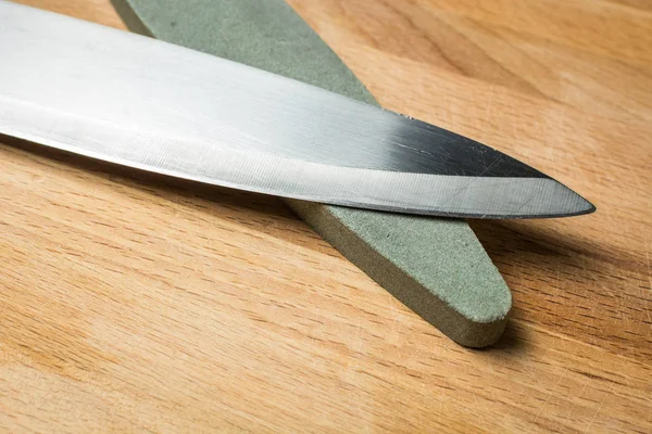 Cuchillo de cocina largo para verduras con muela de abrasivo grueso sobre tabla de madera . —  Fotos de Stock