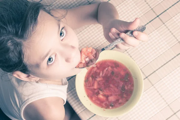 Красивая девушка ест суп из тарелки за кухонным столом ложкой . — стоковое фото
