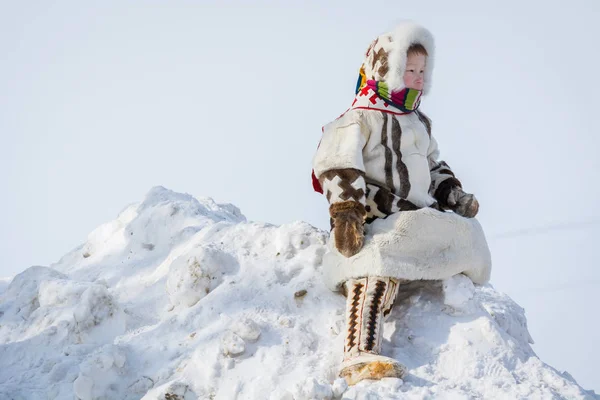 Russkinskaya, Russia - 24 March 2018: Indigenous boy in national northern clothes made of deerskin leather and fur, sits on snowy mountain and looks at the central square from above. Holiday of the re — Stock Photo, Image