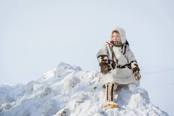 Russkinskaya, Russie - 24 mars 2018 : Garçon sibérien en vêtements nationaux nordiques en cuir et fourrure de cerf, assis sur la montagne de neige, sur la place centrale. Vacances de l'éleveur de rennes . — Photo