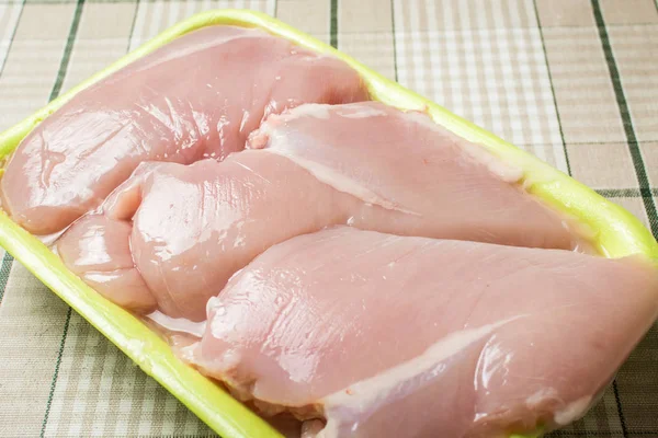 Филе сырой куриной грудки лежит в пластиковой зеленой упаковке на кухонном столе. — стоковое фото