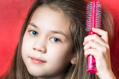 Güzel kız kırmızı bir arka plan üzerinde yuvarlak bir tarak ile saçlarını fırçalar