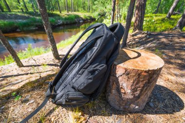 Yaz ormanlarında nehrin arka planına karşı kumlu kıyıda kütük hakkında Spor siyah sırt çantası maliyetleri