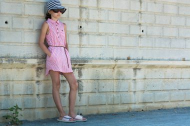 Side, Türkiye - Haziran 2018: Kirli duvarın yanındaki elbise ceplerinde elleri şapkalı ve güneş gözlüğü takan bir kız.