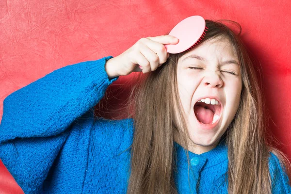 Jolie fille dans un pull bleu peigne ses cheveux et chante sur un fond rouge — Photo