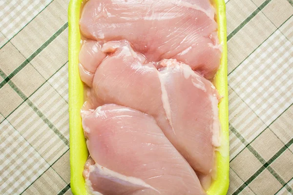 Raw chicken breast fillet lies in plastic green packaging on the kitchen table. — Stock Photo, Image