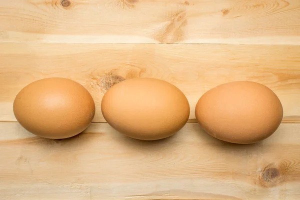 Trois œufs de poulet reposent sur une planche de bois — Photo