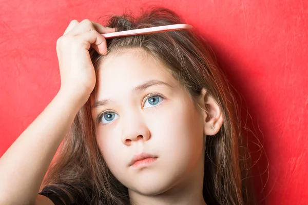 Pensive girl holds a comb in her hair on a red background