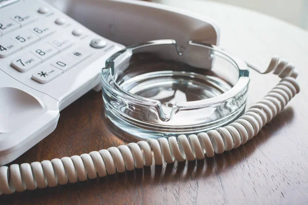Telefone de casa em botões com tubo fora ao lado de cinzeiro de vidro na mesa de madeira . — Fotografia de Stock