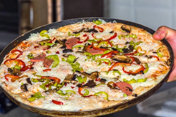 Рука держит тарелку свежеприготовленной пиццы из колбасы, сыра и перца . — стоковое фото