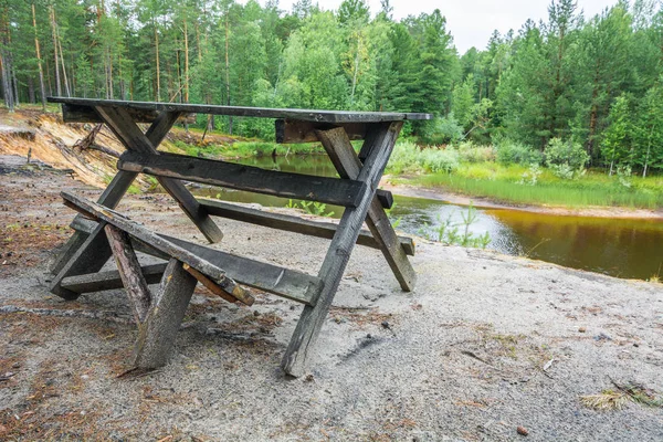 Forest camp for rest with bench and table in forest against taiga river.