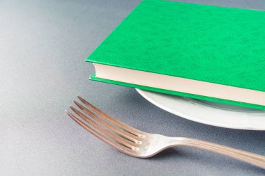 Yeşil kitap çatalın yanında beyaz bir tabakta yatıyor.