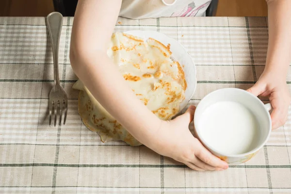 Руки ребенка берут кружку молока, чтобы смыть блины . — стоковое фото