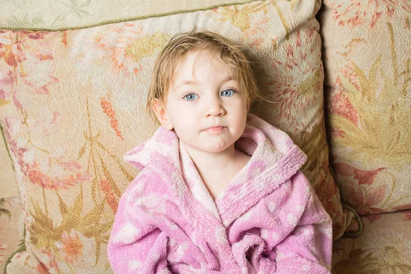 Cute baby with wet hair after bath in bathrobe dries on sofa. — Stock Photo, Image