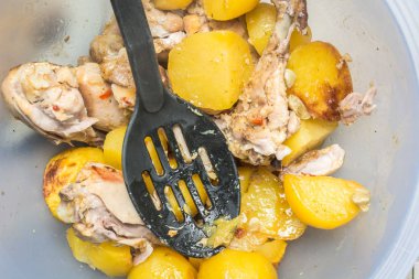 Pişmiş tavuk bacakları ve mutfak masasında büyük tabakta kepçe ile dilimlenmiş patates.