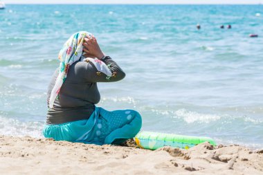 Side, Türkiye - 02 Haziran 2018: Başında mendil olan giyinmiş kadın sahilde dinleniyor ve mavi denizde mesafeye bakıyor.