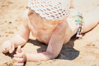 Beyaz güneş şapkalı güzel bebek kumlu plajda yatıyor ve oynuyor