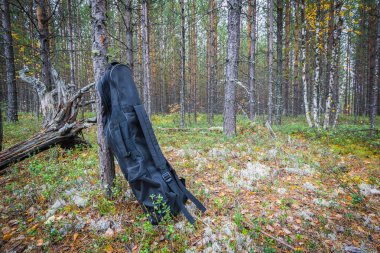 Metal dedektörü için siyah büyük kapalı çanta sonbaharda ağaçlar arasında orman kenarında duruyor.