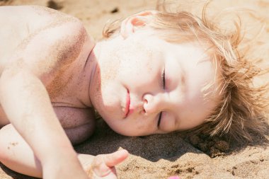 Küçük çocuk sıcak kumda gözleri güneşte kapalı güneşlenince güneşlenikar