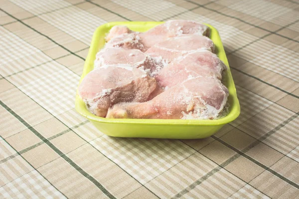 Frozen chicken legs for cooking in green plastic container on the kitchen table. — Stock Photo, Image