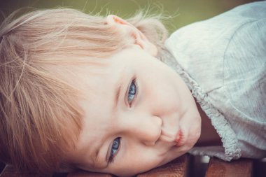 Parlak giysiler içinde memnun çocuk yalan ve şehir parkında uzun bankta dinleniyor