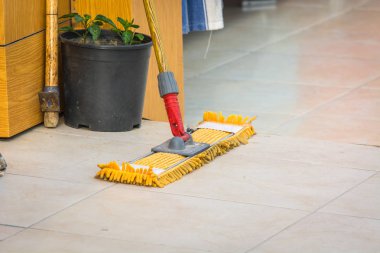 Wooden mop with large yellow pile for washing floors on tile