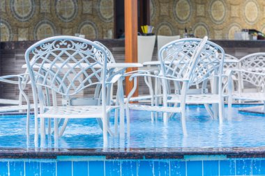 Bar sayacının arka planında mavi havuzlu sandalyelerle yemek masası