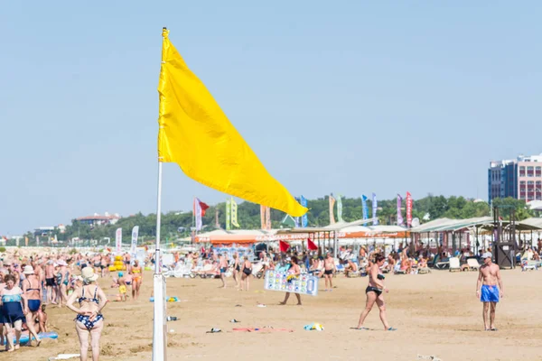 LADO, TURQUÍA - 02 DE JUNIO DE 2018: Bandera amarilla en la playa de arena con gente descansando . —  Fotos de Stock