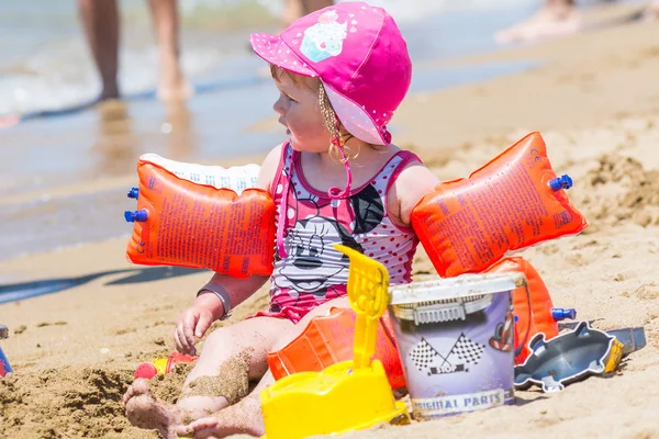 Seite, Truthahn - 2. Juni 2018: Schönes Mädchen mit Mütze und aufblasbaren Armbinden sitzt neben Sandspielzeug am Strand. — Stockfoto