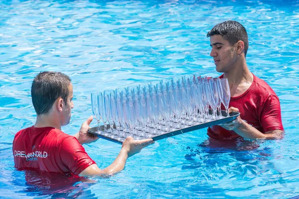 SIDE, TURKEY - ИЮНЬ 2, 2018: Мужчины в красных футболках несут поднос с пустыми бокалами шампанского в бассейне . — стоковое фото