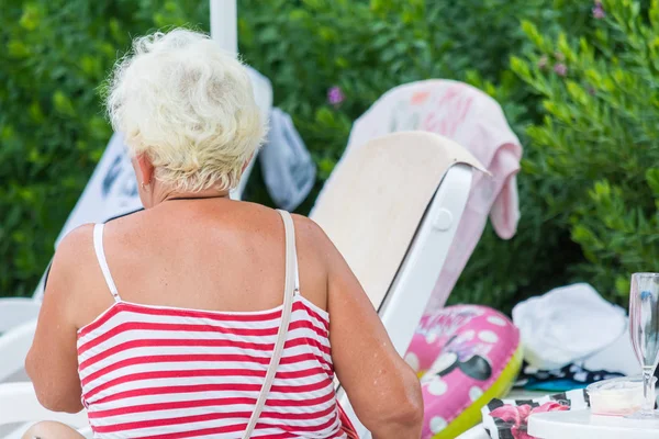 LADO, TURQUÍA - 2 DE JUNIO DE 2018: Anciana con camisa a rayas sentada en la tumbona junto a la piscina . — Foto de Stock
