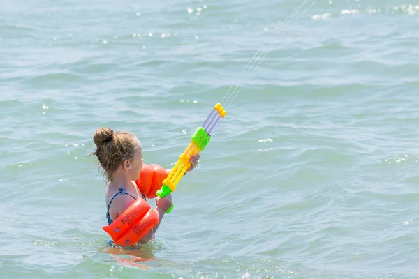 LATO, TURCHIA - 31 MAGGIO 2018: Bambina in costume da bagno e maniche spruzza acqua da pistola ad acqua in mare . — Foto Stock