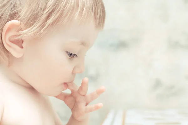 Bright child with blue eyes sucks her finger on her hand. — Stock Photo, Image