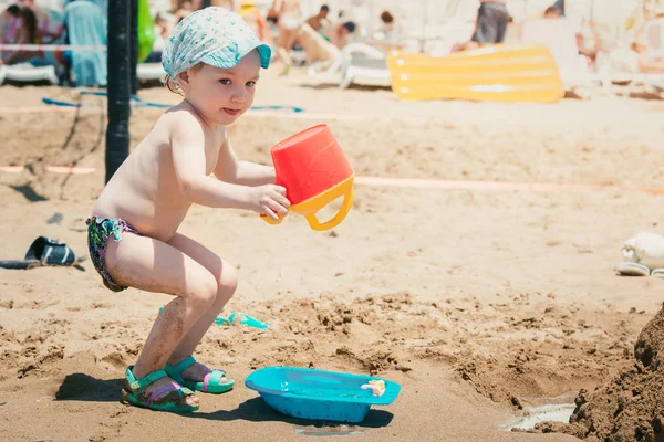 Lustiges Baby in Sommermütze spielt mit Spielzeug am Sandstrand. — Stockfoto