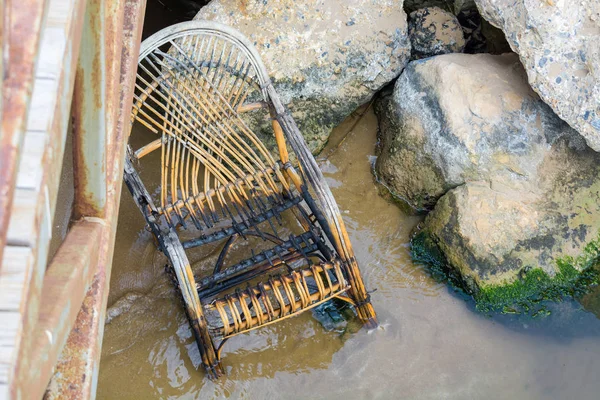 Leégett fonott szék áll River bank közelében kövek alatt híd. — Stock Fotó