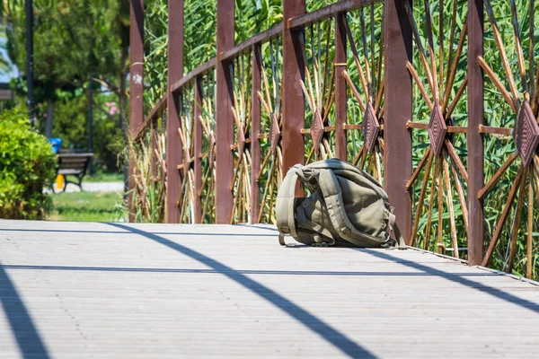 Green hiking backpack for fishing lies on wooden bridge over river in park.