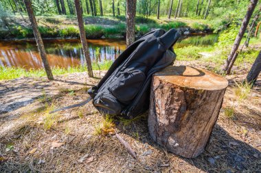 Yaz ormanlarında nehrin arka planına karşı kumlu kıyıda sarı kütük hakkında Spor siyah sırt çantası maliyetleri.