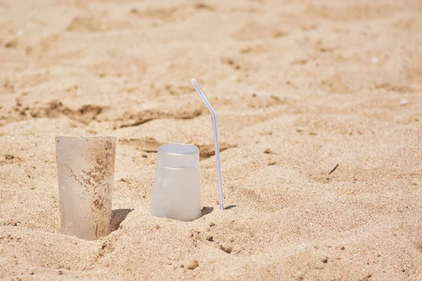 Leere Plastikbecher und Schläuche an sandigem Meeresufer liegen gelassen. — Stockfoto