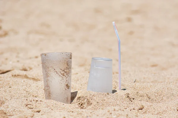 Leere Plastikbecher und Schläuche an sandigem Meeresufer liegen gelassen. — Stockfoto