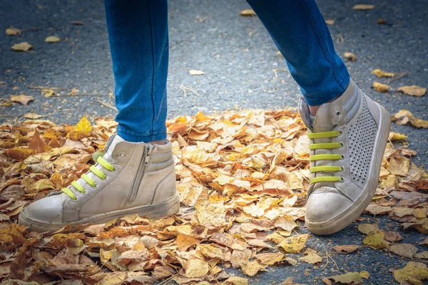 Beine eines Kindes mit Turnschuhen und grünen Schnürsenkeln zum Laufen auf gelben Blättern an einem Herbsttag. — Stockfoto
