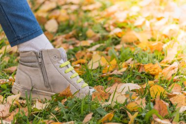 Bir sonbahar gününde sarı yapraklar üzerinde çalışan bebek spor ayakkabıları ve yeşil bağcıklar ile çocuk bacağı.