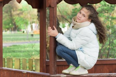 Bir sonbahar gününde çardak üzerinde oturan aşağı ceket sevimli kız.
