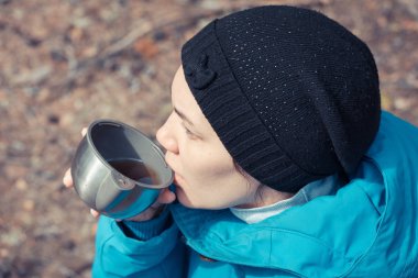 Ormanda yürüyüş yaparken ısınmak için kızın elinde çay olan termostan bir kupa çay..