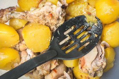 Pişmiş tavuk bacakları ve mutfak masasında büyük tabakta kepçe ile dilimlenmiş patates.