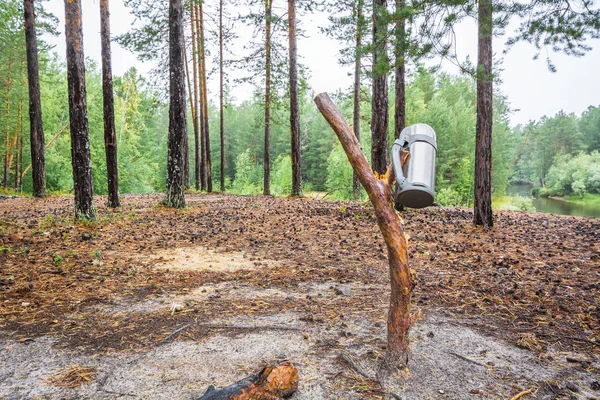 Schwere Marschthermoskanne für heißen Tee oder Kaffee hängt am Holzstab im Wald vor dem Hintergrund der Taiga. — Stockfoto