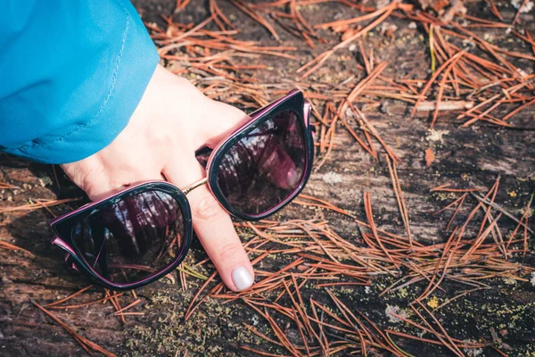 Womens sunglasses with dark lenses in the hands of the girl with finger depicting the nose in the forest.