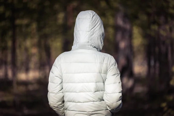 Девушка в светлой куртке с капюшоном стоит и смотрит в глубины соснового леса . — стоковое фото